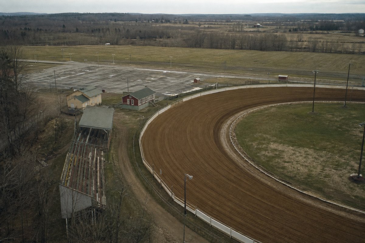 An elevated view of a small racing oval and its barn area, the dirt surface freshly harrowed
